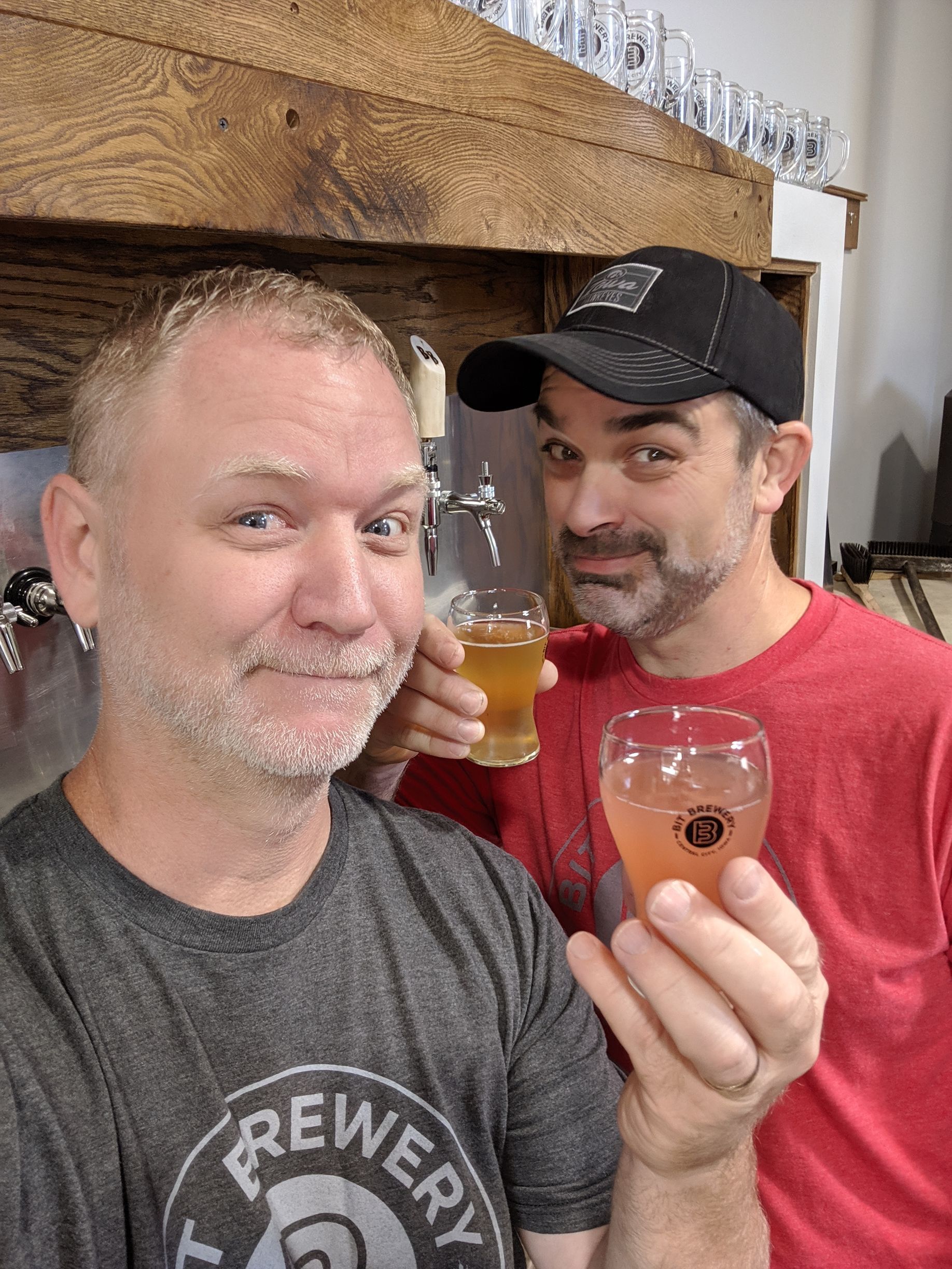 Scott and Jason are standing next to each other holding glasses of beer.
