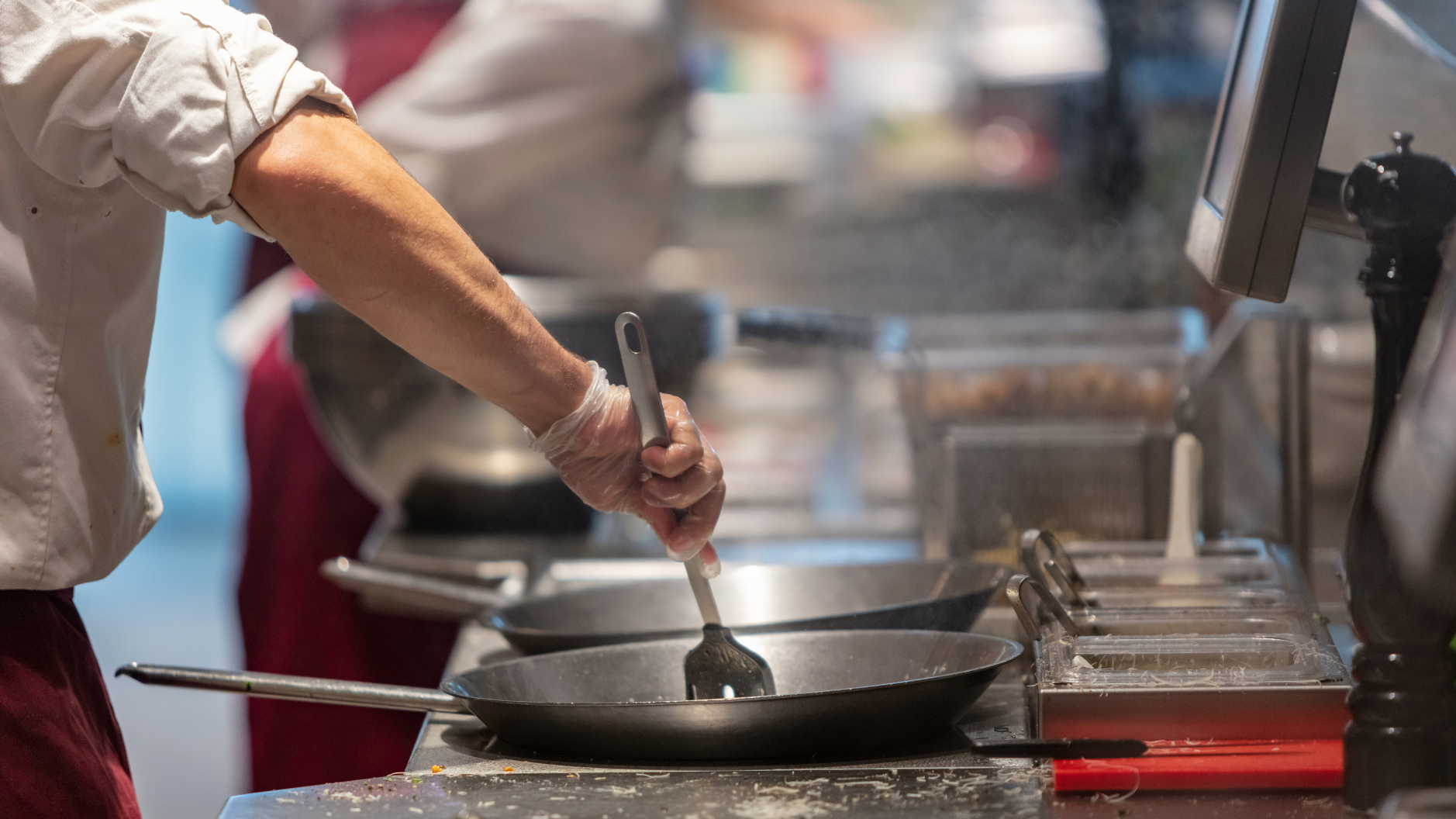 Chef stirring contents in a pan with a spatula, in a commercial kitchen.