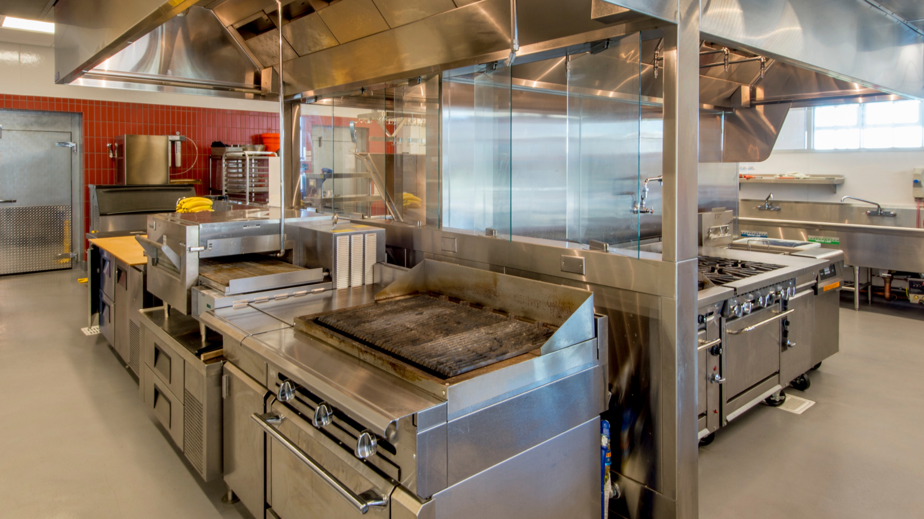 Commercial kitchen with stainless steel appliances and ventilation hoods.