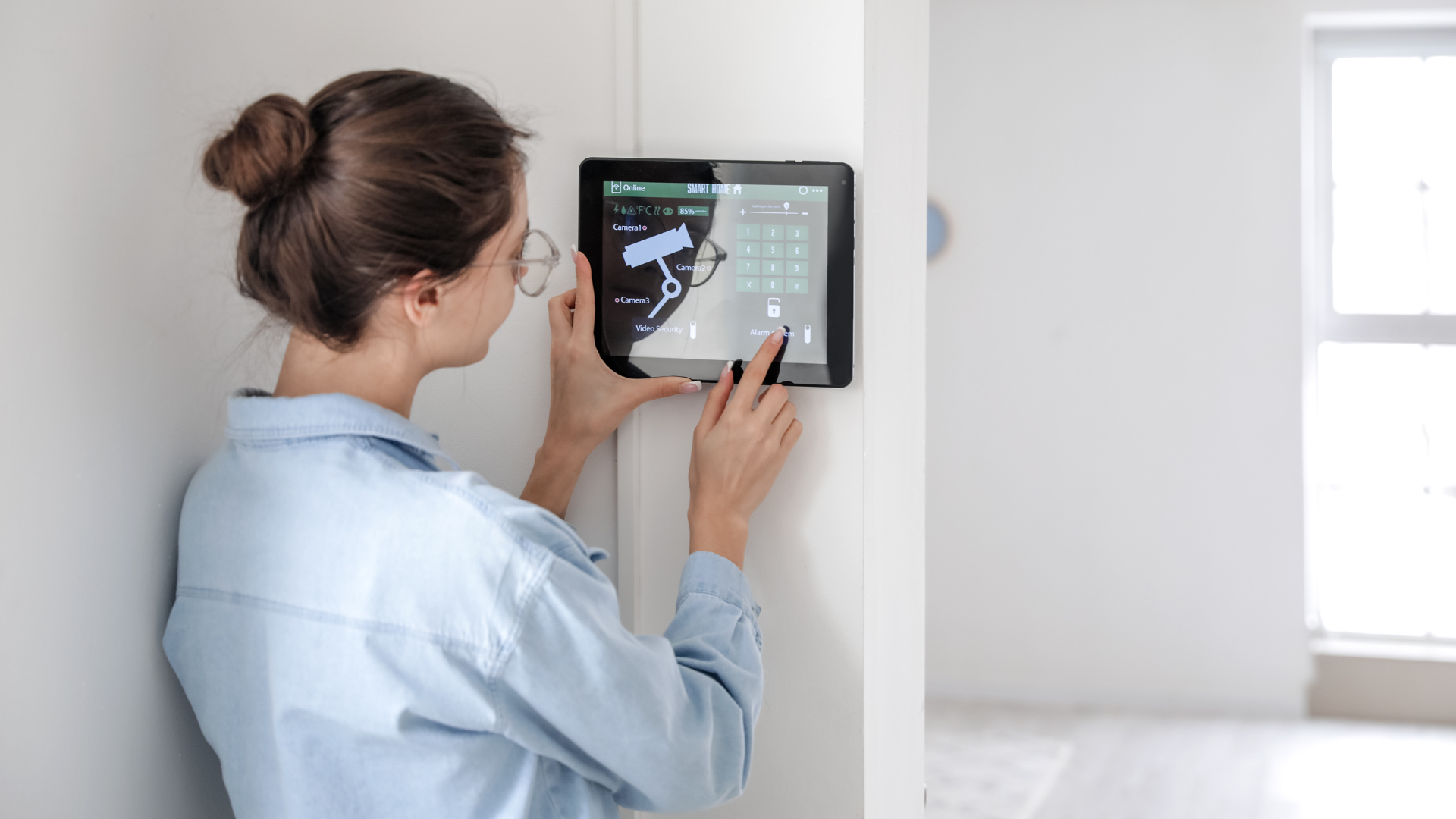 Hand touching a blue touchscreen thermostat on a wall, with weather and menu options displayed