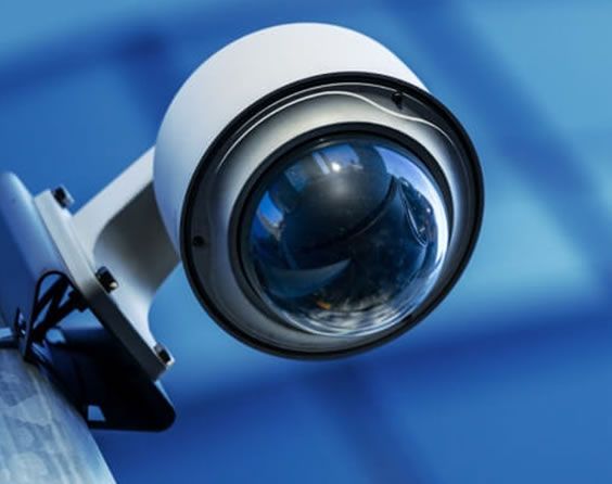 Close-up of a white security camera with a blue lens on a blue background
