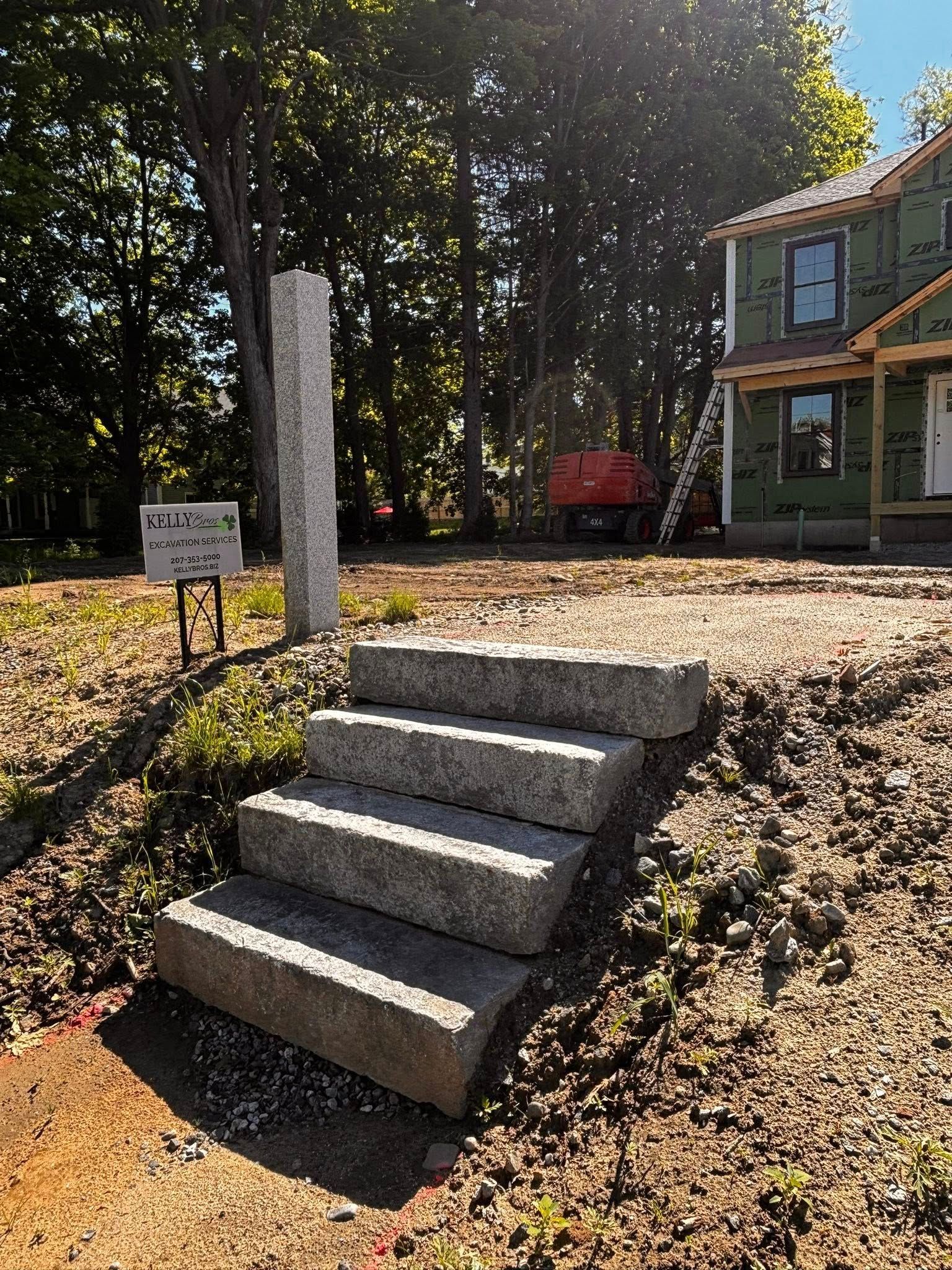 Concrete steps leading up a grassy embankment to a house with trees and a red trailer in the background