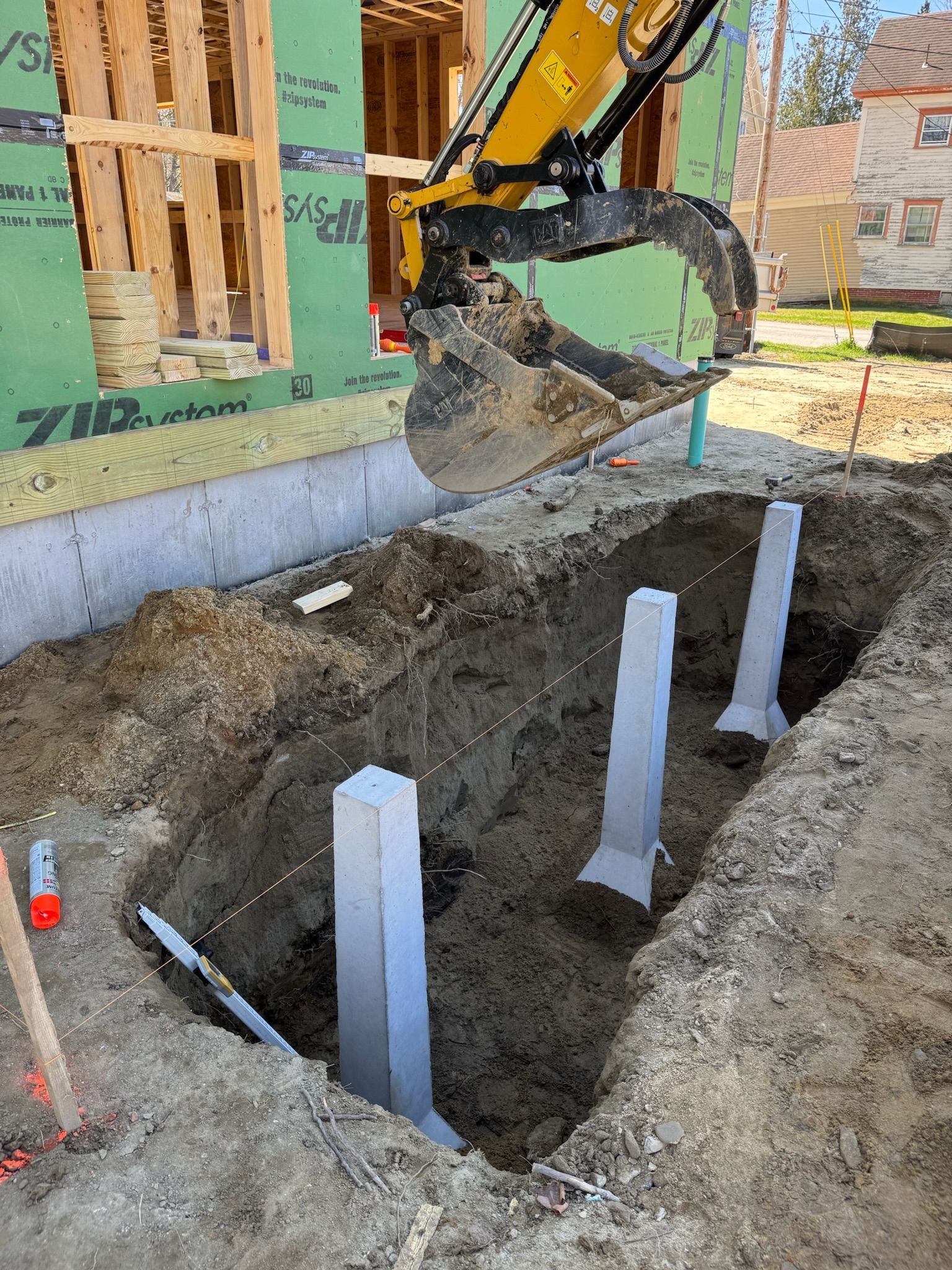 Excavator digging around white support posts beside a house foundation under construction