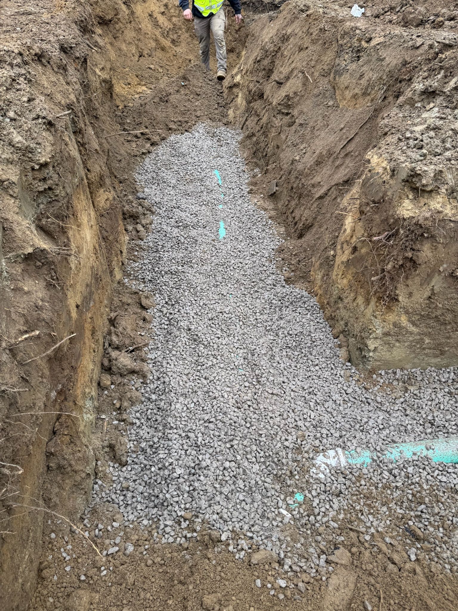 Trenched dirt pit filled with gray gravel, with a worker partially visible at the top.