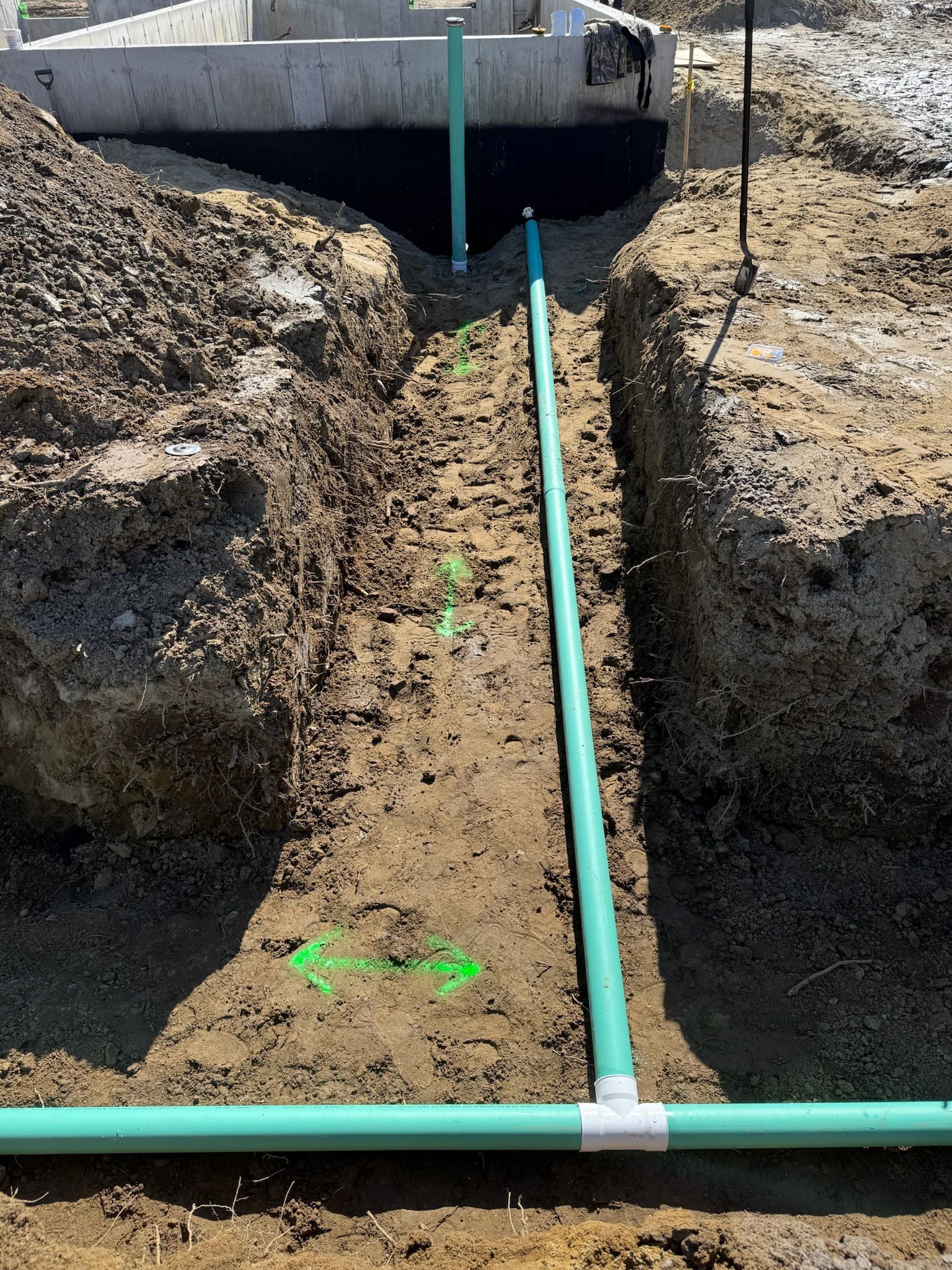 Green PVC pipes laid in a dirt trench beside a concrete structure under construction