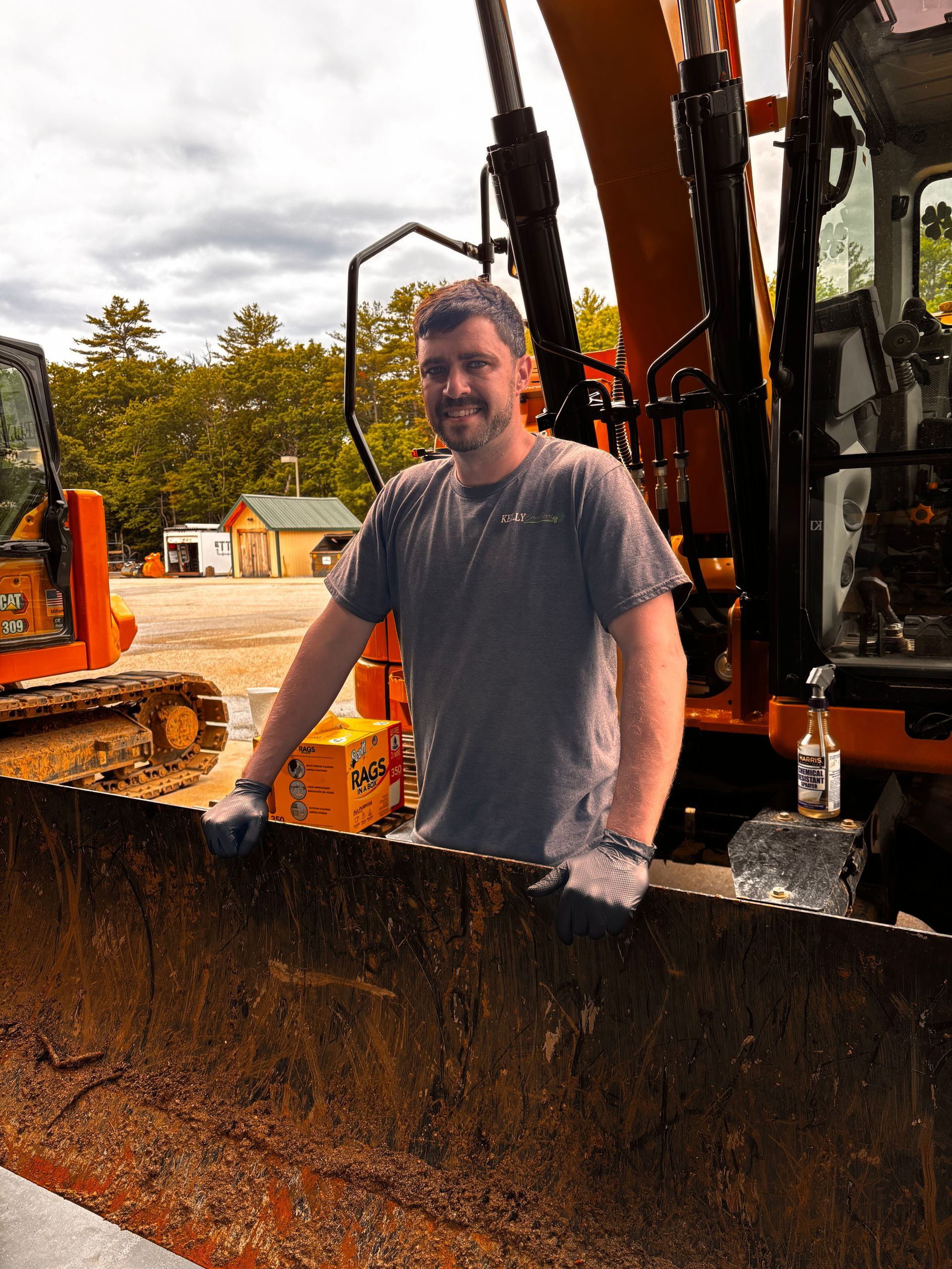 Man standing in an orange excavator bucket at a construction site, smiling at the camera.