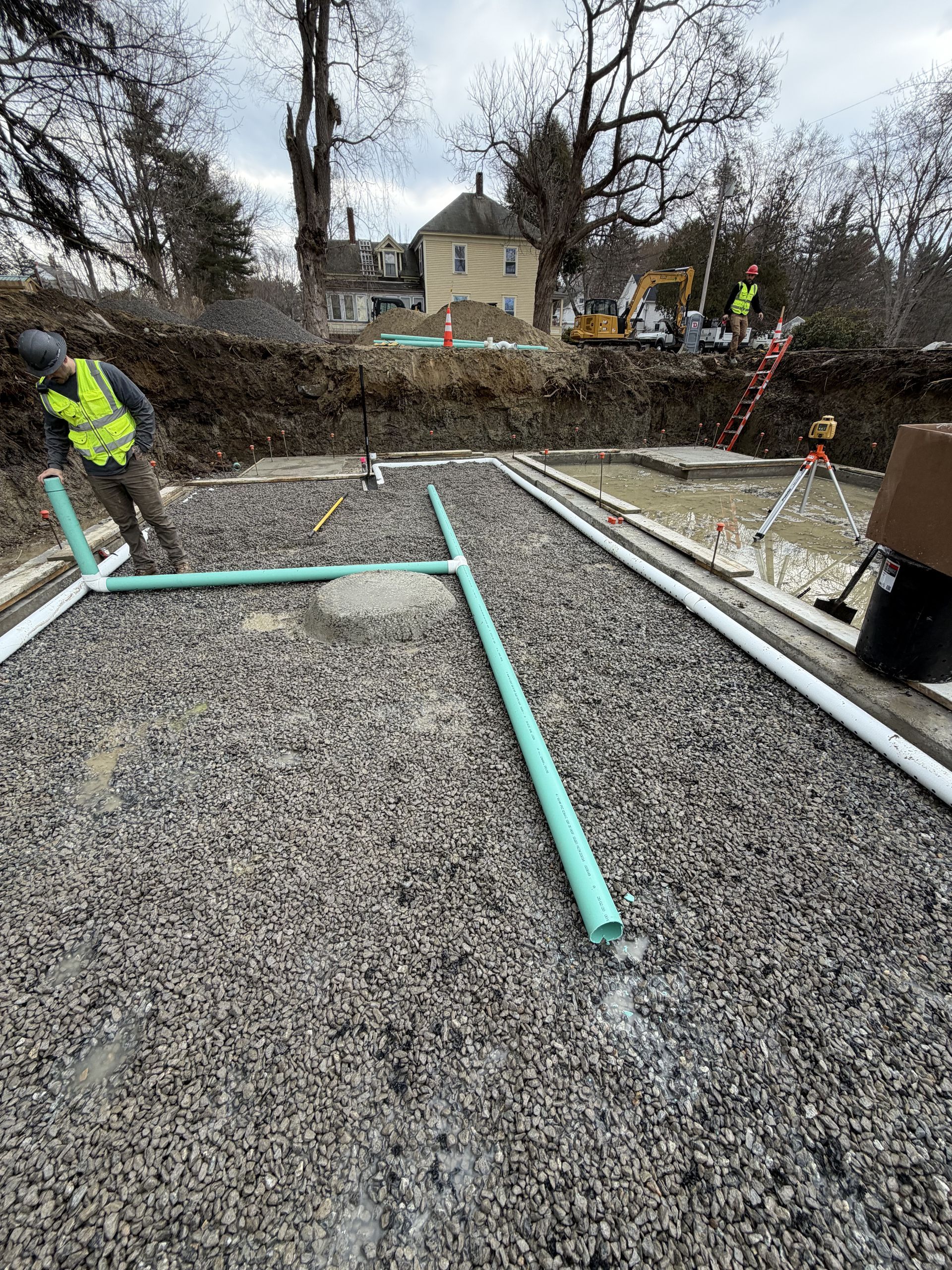 Construction workers laying turquoise pipes in a gravel foundation trench at a house site