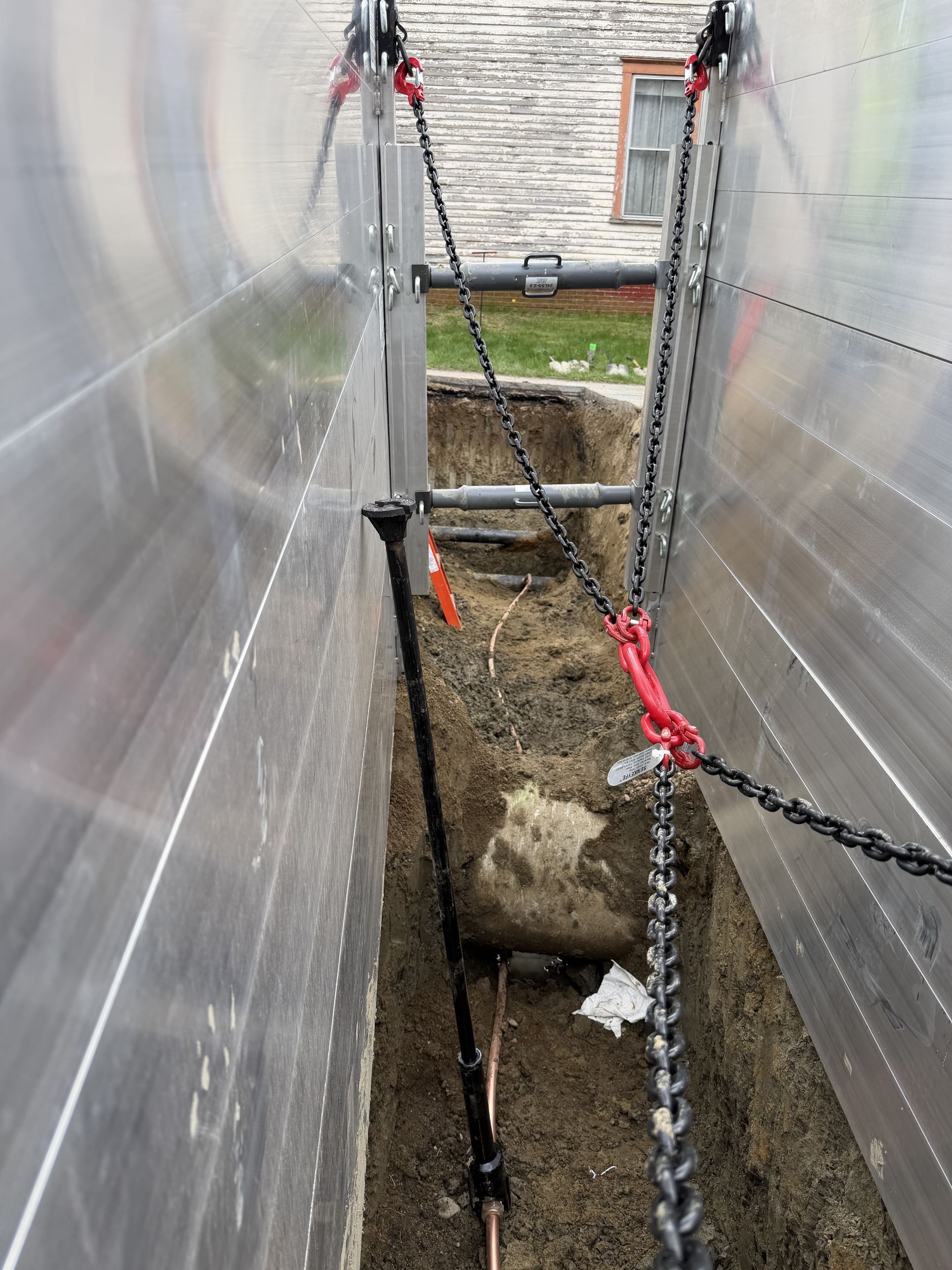 Narrow gap between silver tanks with chains, scaffolding, and a muddy trench below.