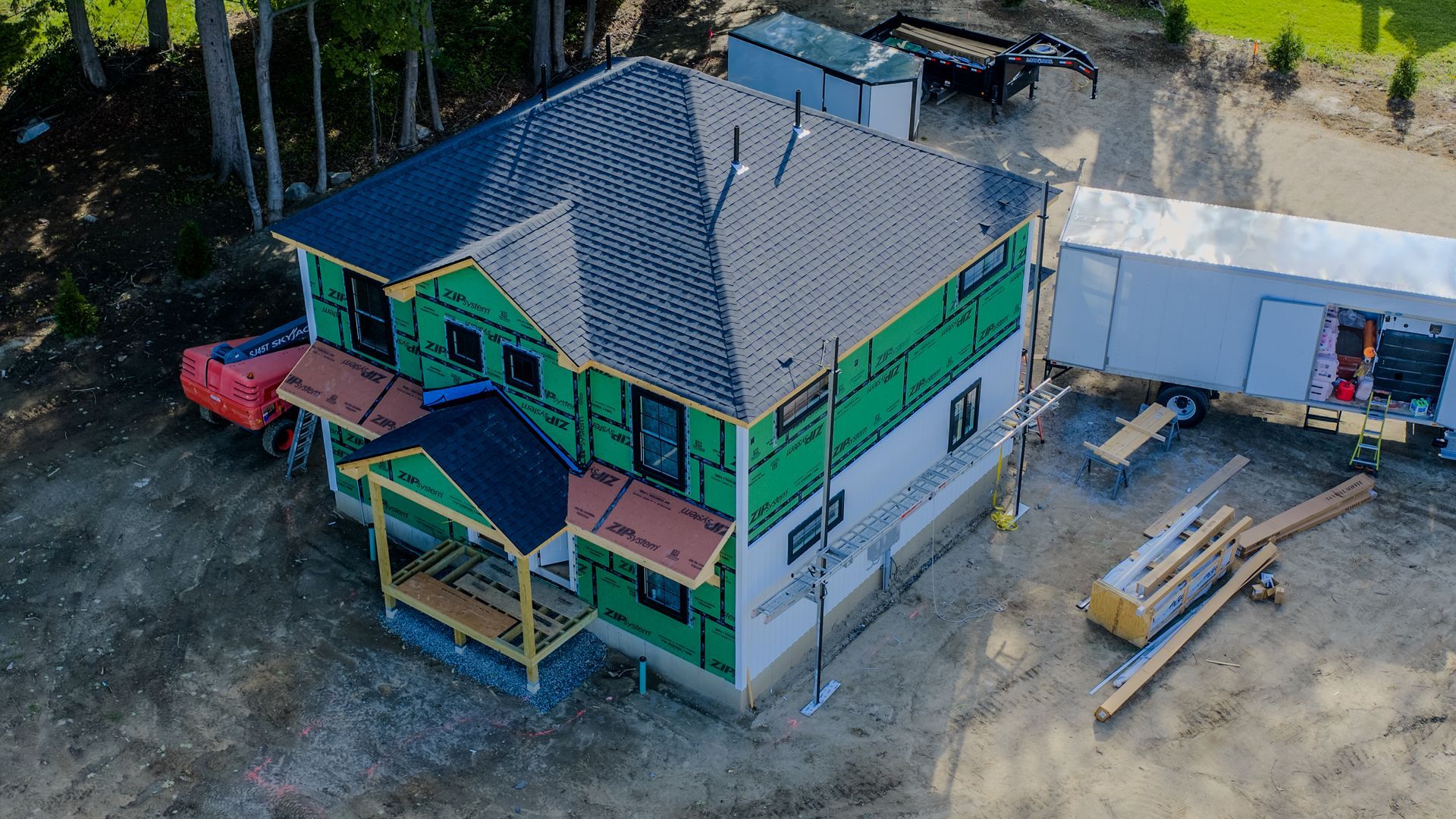 Colorful two-story house under construction with green trim, a gray roof, and a white trailer nearby