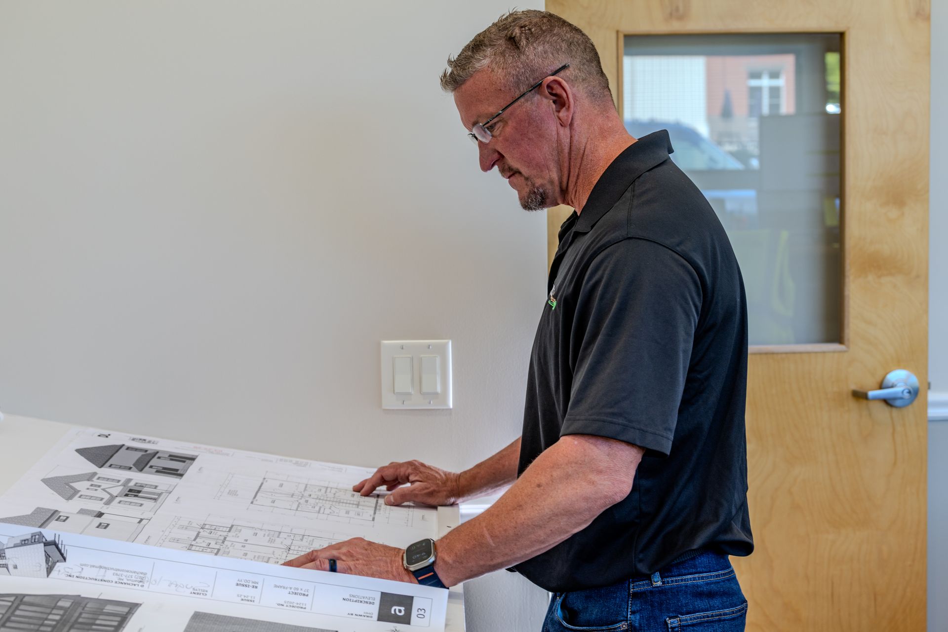 Scott Kelly of Kelly Brothers Excavation in Maine reviewing large blueprints on a table in a bright office room