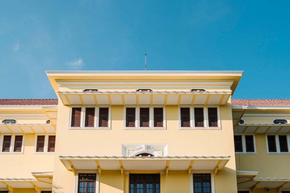 Cream-colored building facade with rows of windows and red-tiled roof against a blue sky