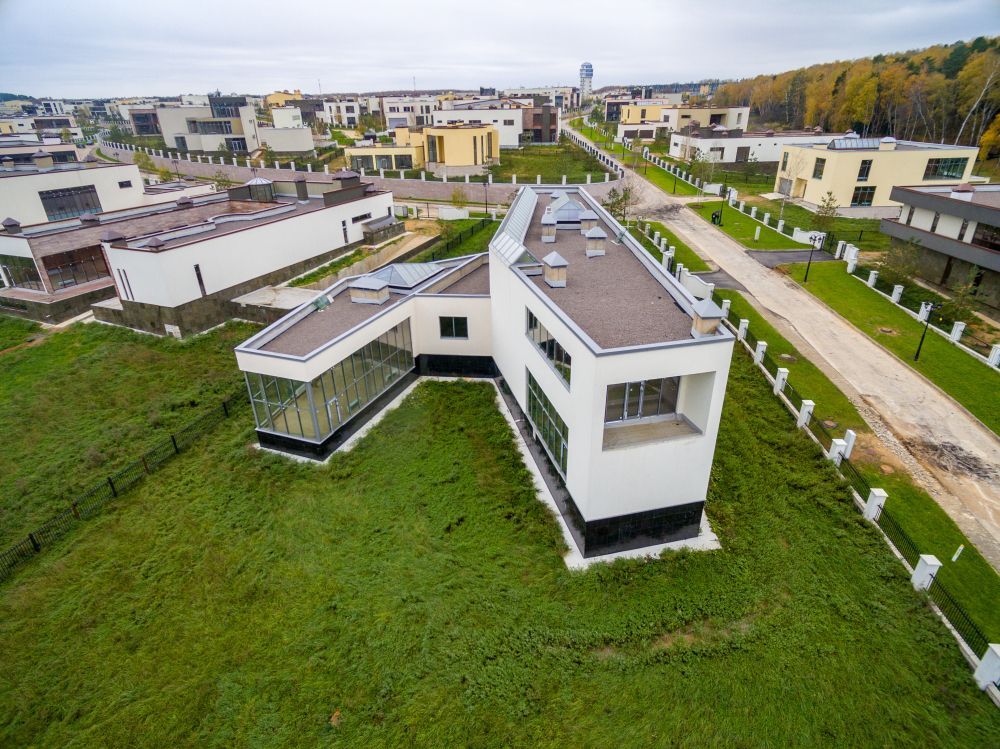 Aerial view of a modern white house with a flat roof in a grassy suburban neighborhood
