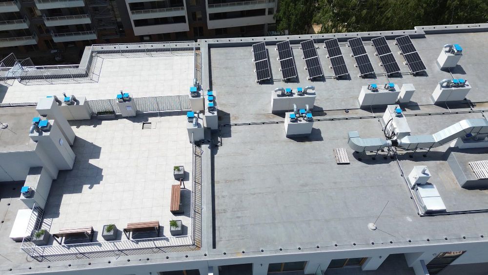 Rooftop with HVAC units and solar panels on a flat commercial building, viewed from above.