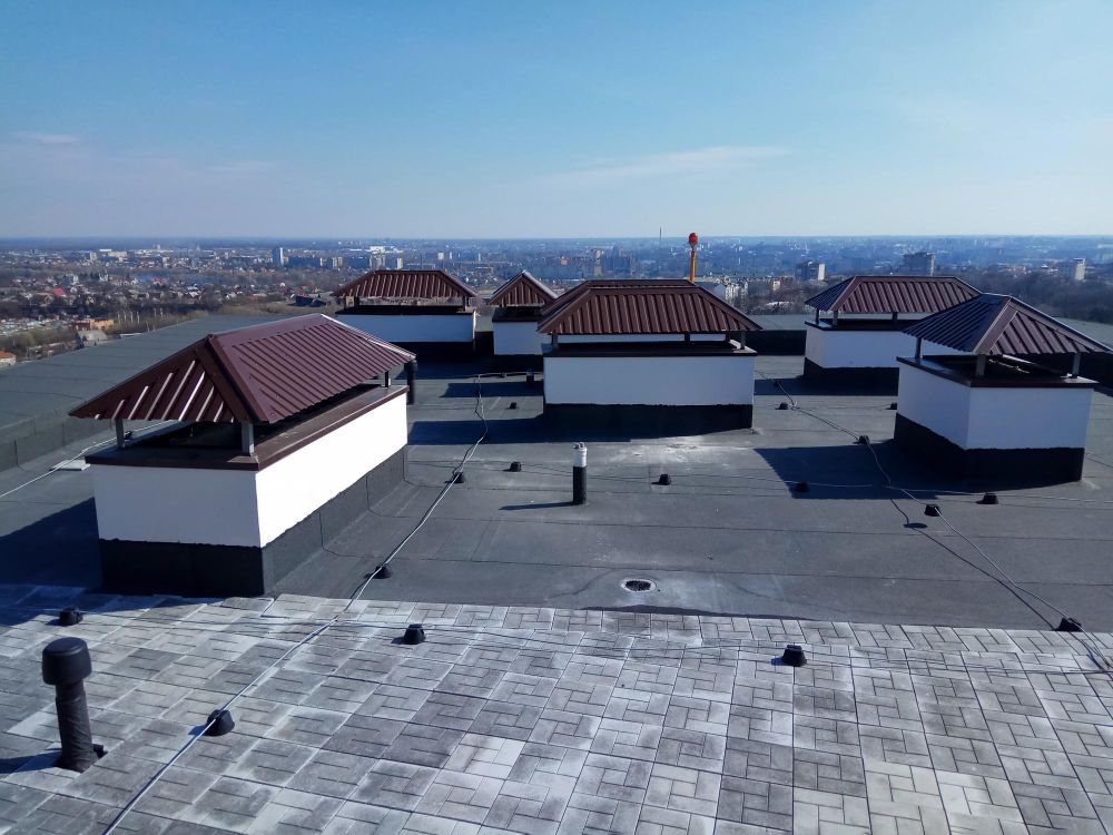 Rooftop with white structures and red tile roofs under a clear sky, overlooking a distant city skyline