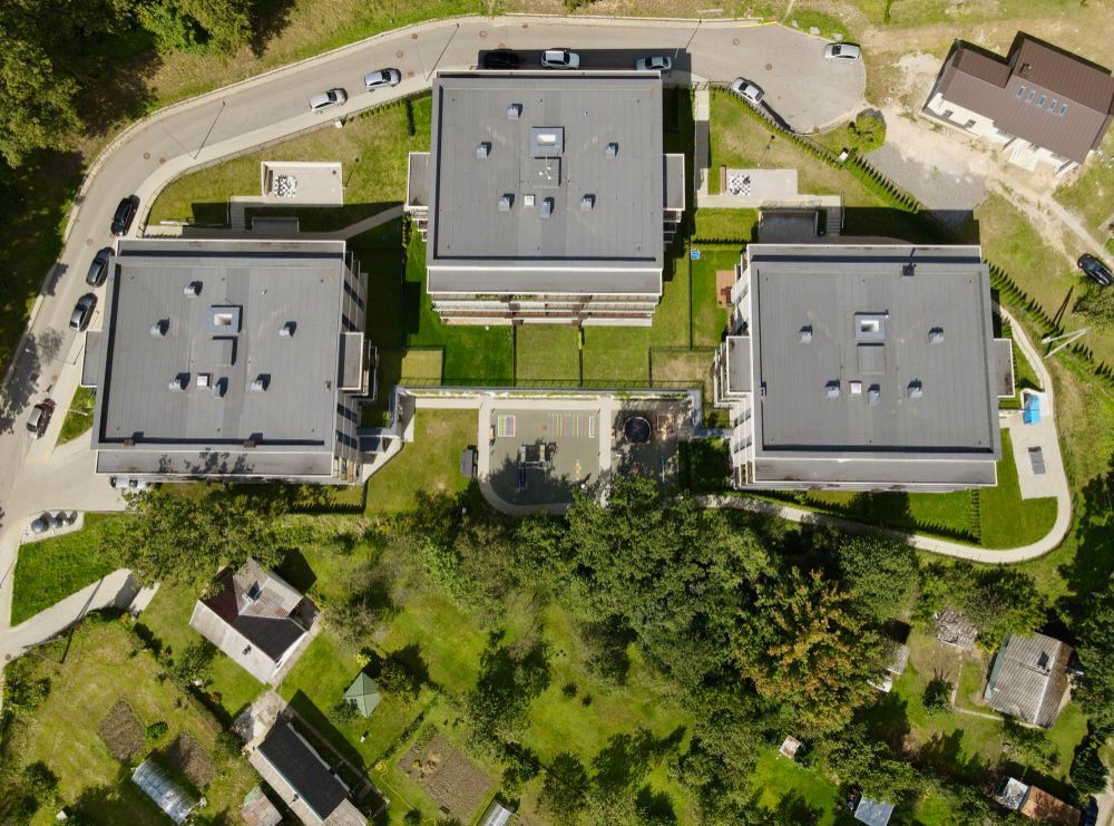 Aerial view of three modern gray-roofed apartment buildings surrounded by green lawns and trees.