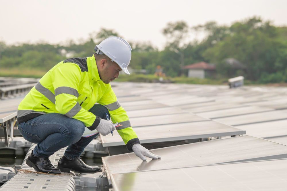Worker in a hard hat and neon jacket installing rooftop solar panels.
