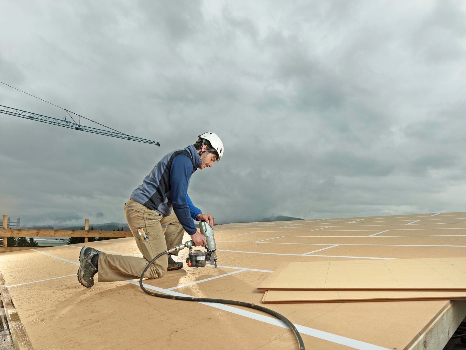 Worker using a power tool on a rooftop under cloudy skies