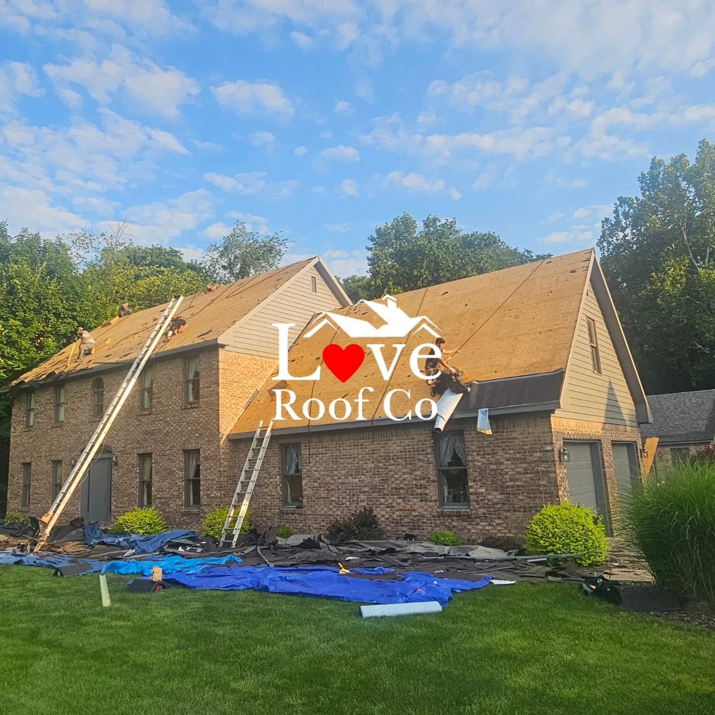 Brick house with roof undergoing installation under blue sky, roofing materials on lawn, Love Roof Co. watermark