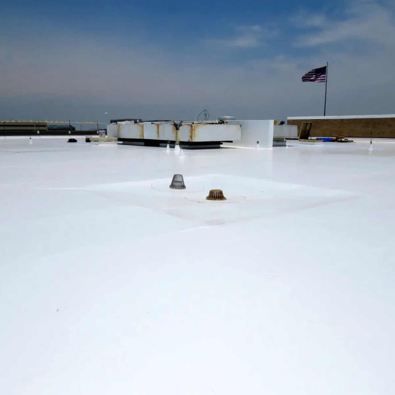 White flat roof with two small vents and a U.S. flag against a clear sky