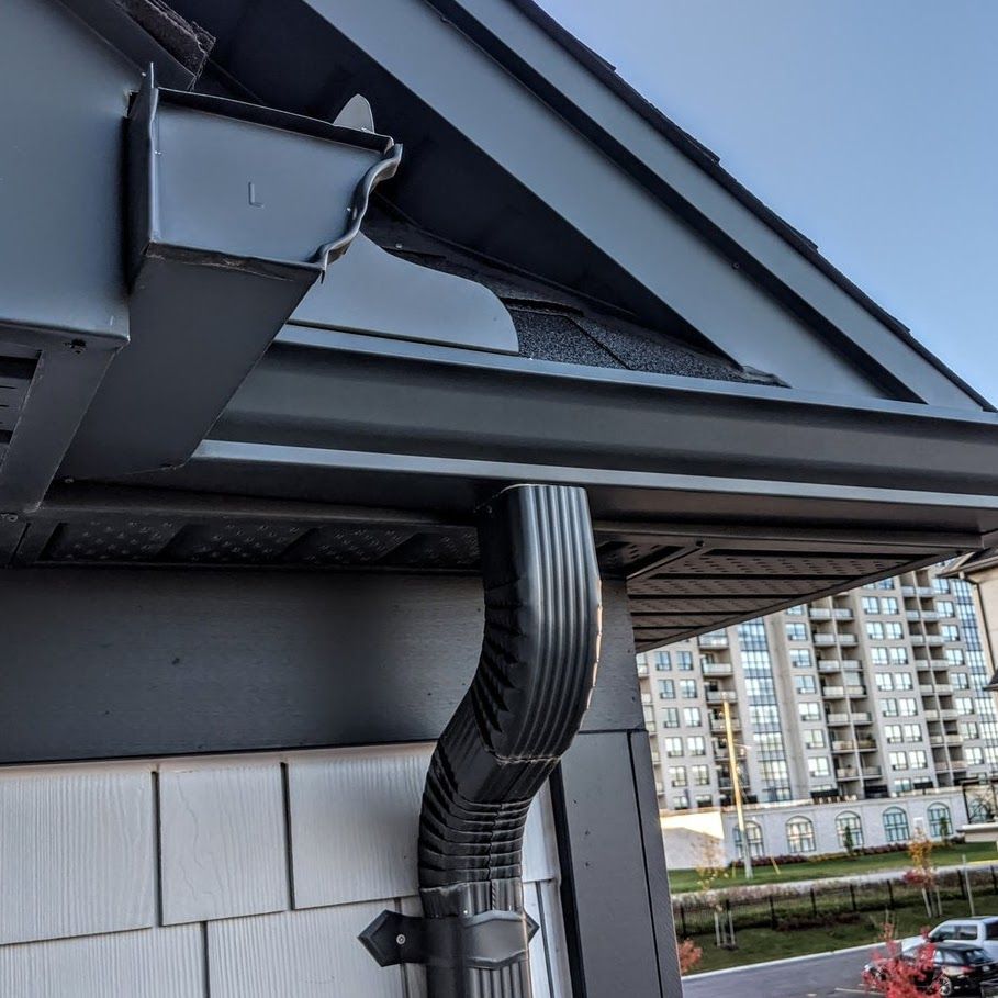 Damaged roof gutter and bent black downspout on a building exterior with apartments in the background