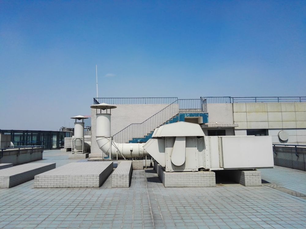 Rooftop HVAC ducts and vents on a flat industrial roof under a clear blue sky
