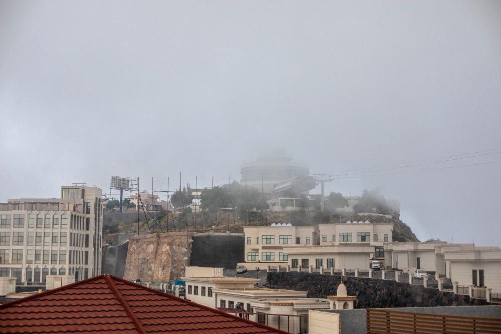 Foggy hillside cityscape with buildings and red-tiled rooftops under a gray sky