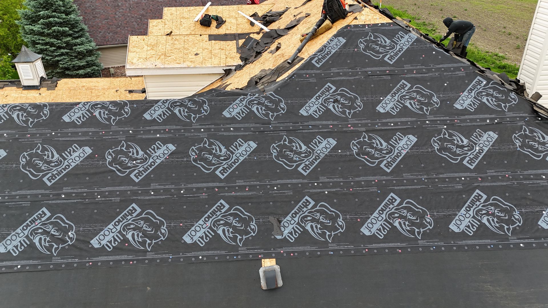 Roof under construction with black underlayment, stacked shingles, and tools near the ridge line