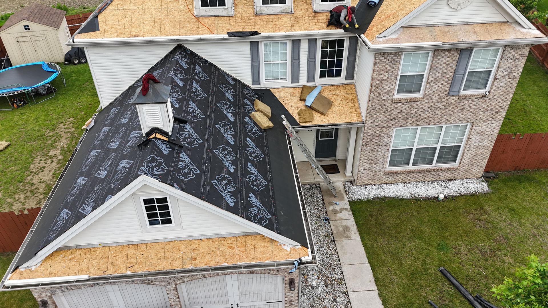 Aerial view of a house roof being repaired, with black underlayment and a few workers on the roof.