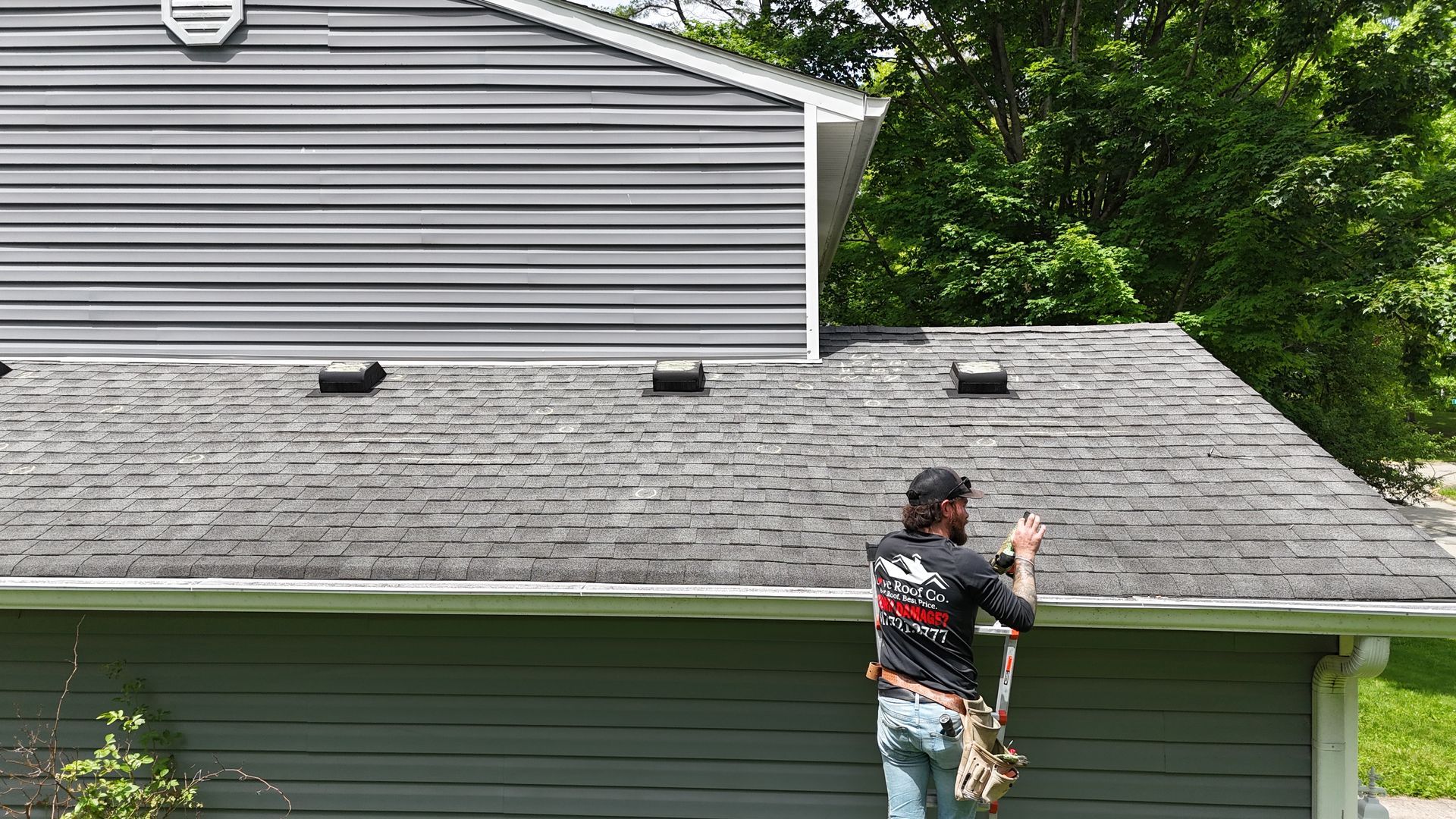 Worker on a roof repairing gray shingles on a house