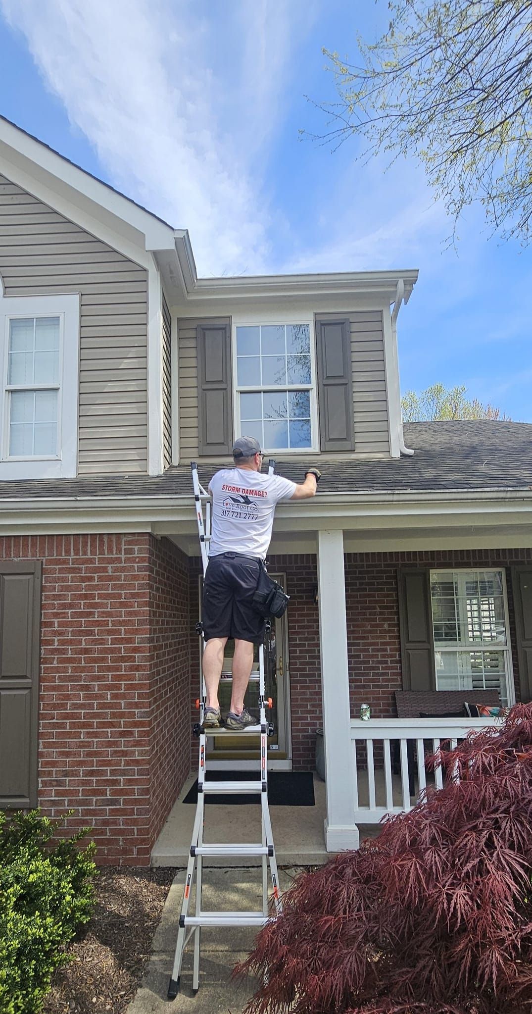 Person on a ladder repairing the roof of a two-story house on a sunny day