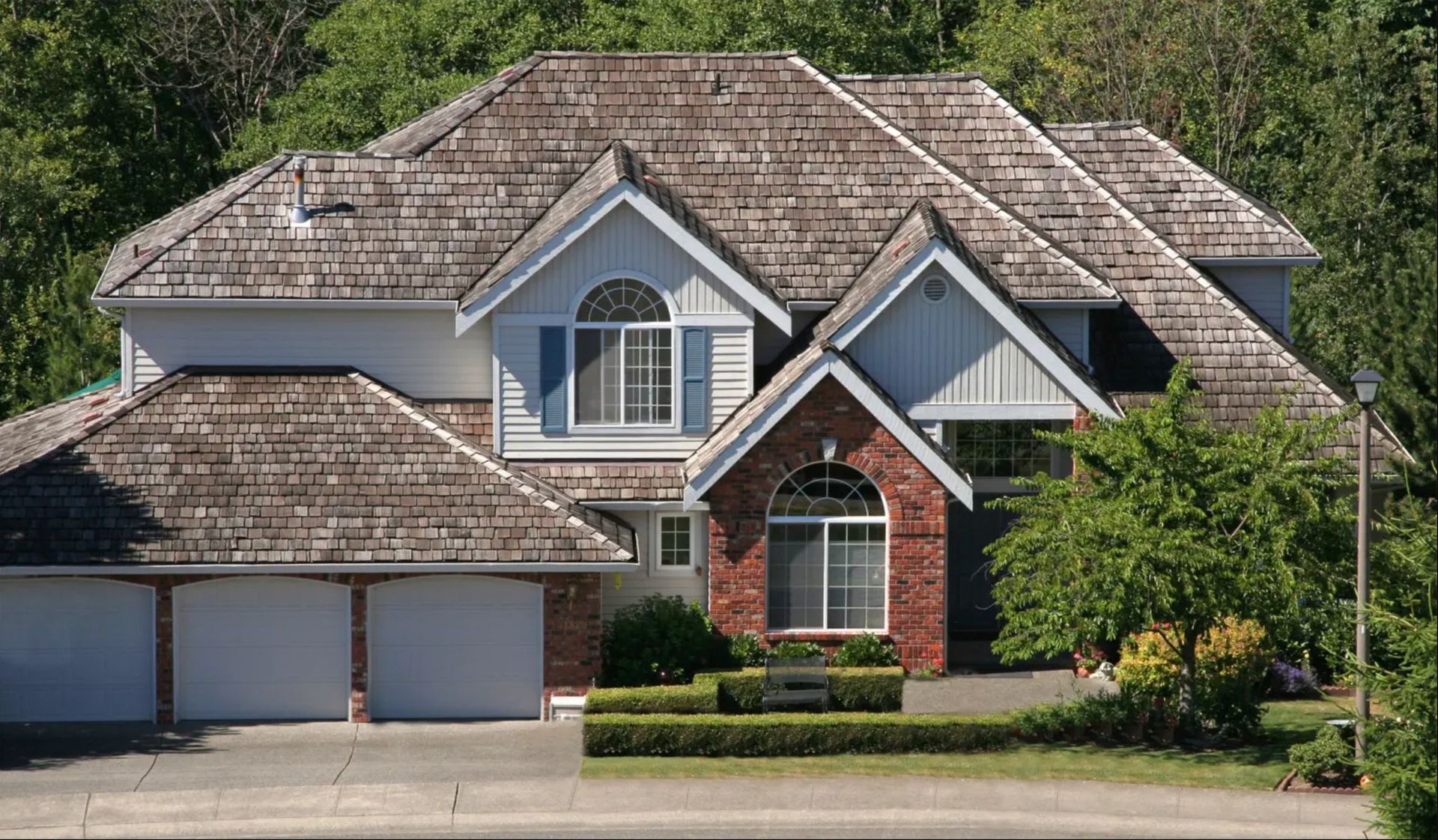 Suburban house with gray roof, brick accents, two garage doors, and a front tree-lined yard