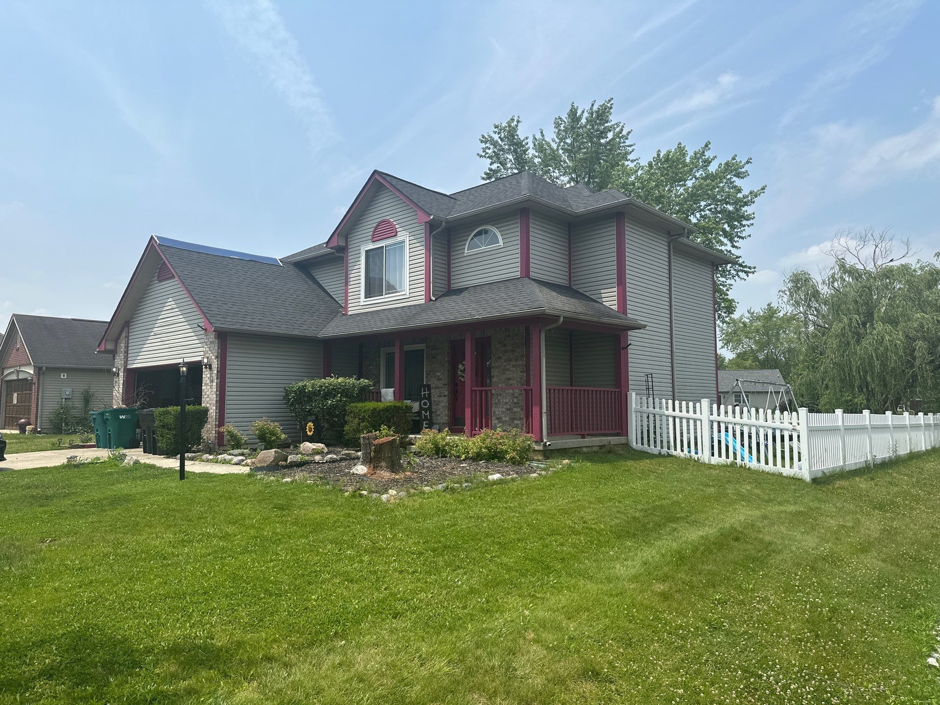Two-story gray house with pink trim, white picket fence, and a green front lawn under a cloudy sky