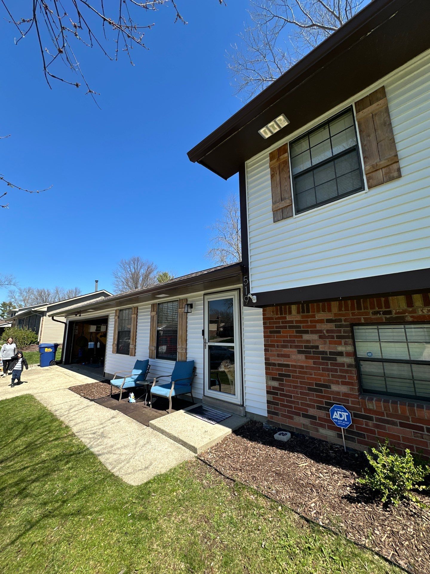 Exterior of a brick-and-white building with blue chairs, a sidewalk, and a bright blue sky
