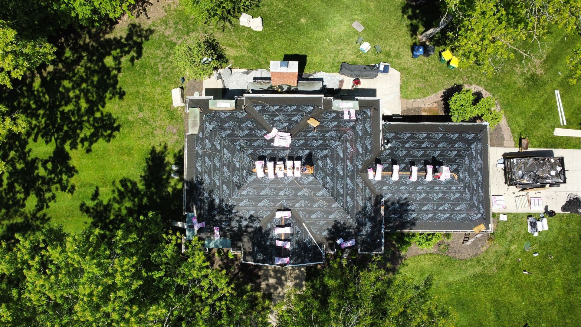 Aerial view of a house undergoing roof replacement surrounded by green trees and lawn
