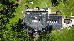 Aerial view of a house undergoing roof replacement surrounded by green trees and lawn