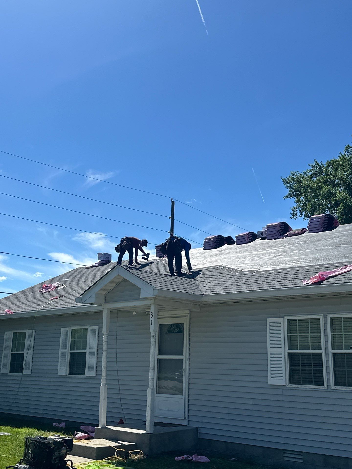 Workers on a gray shingle roof repairing a house under a clear blue sky.