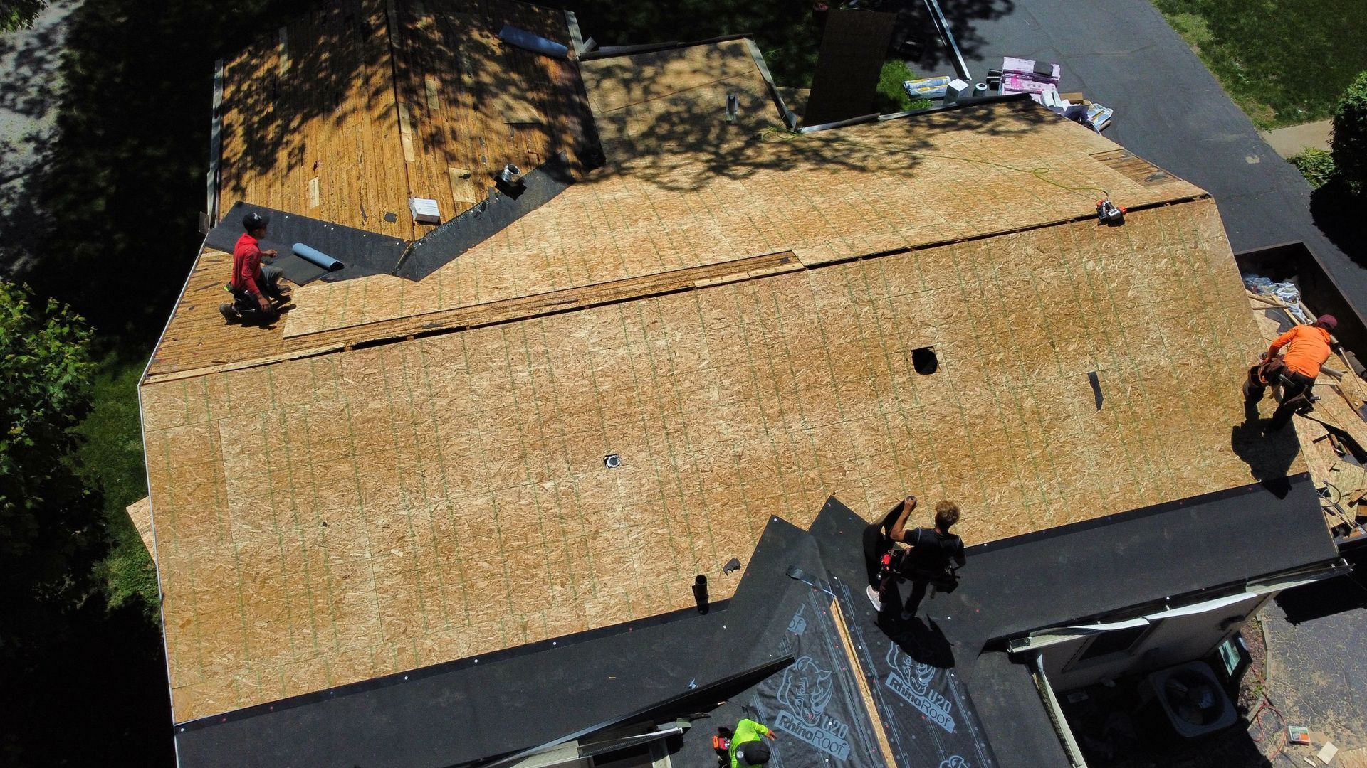 Workers on a roof with roofing materials and equipment visible.