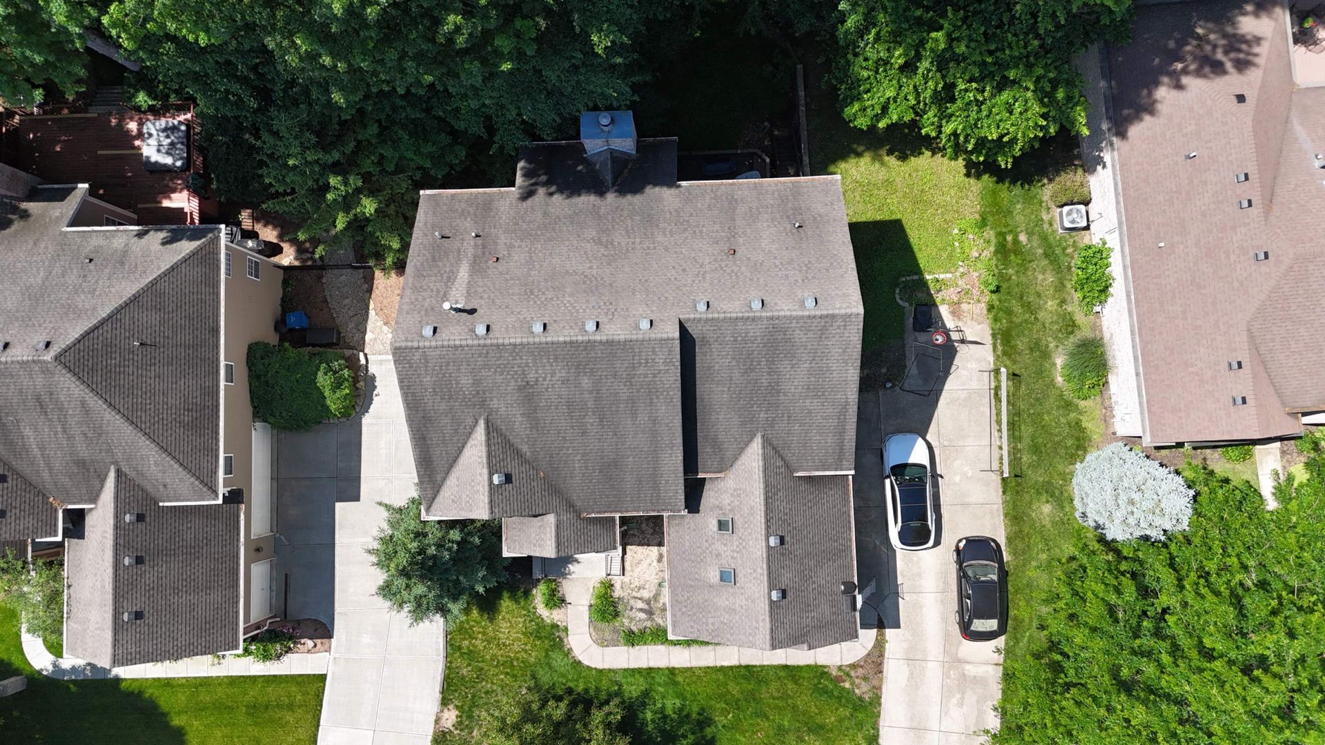 Aerial view of a suburban house with driveway, parked cars, and green lawn