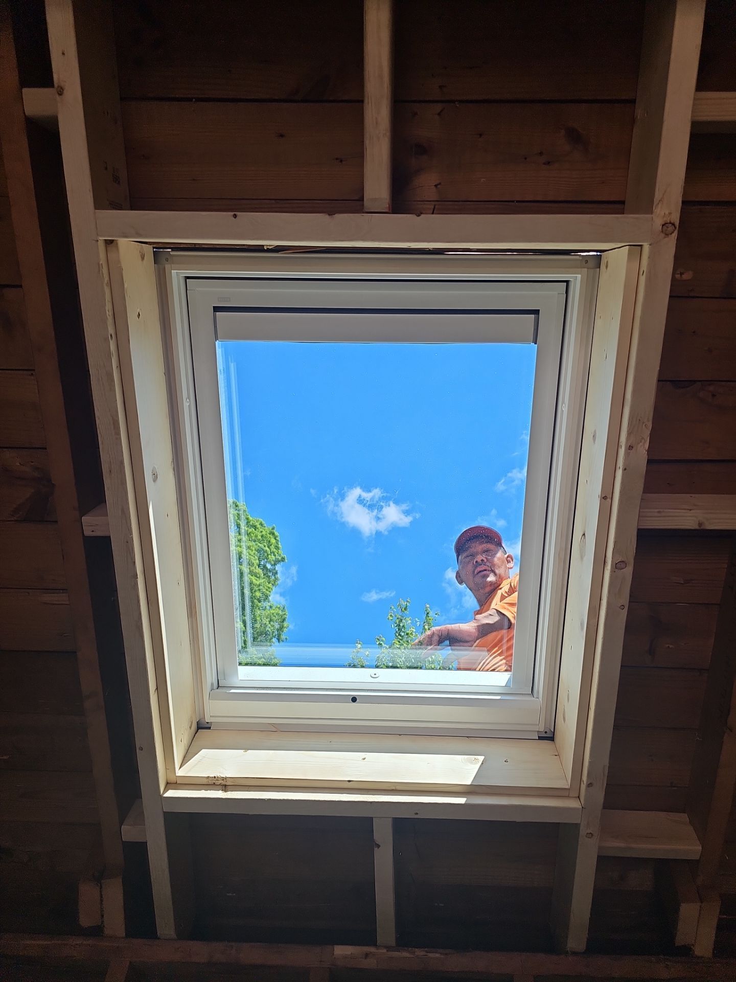 Person looking down through an open attic skylight to a bright blue sky.