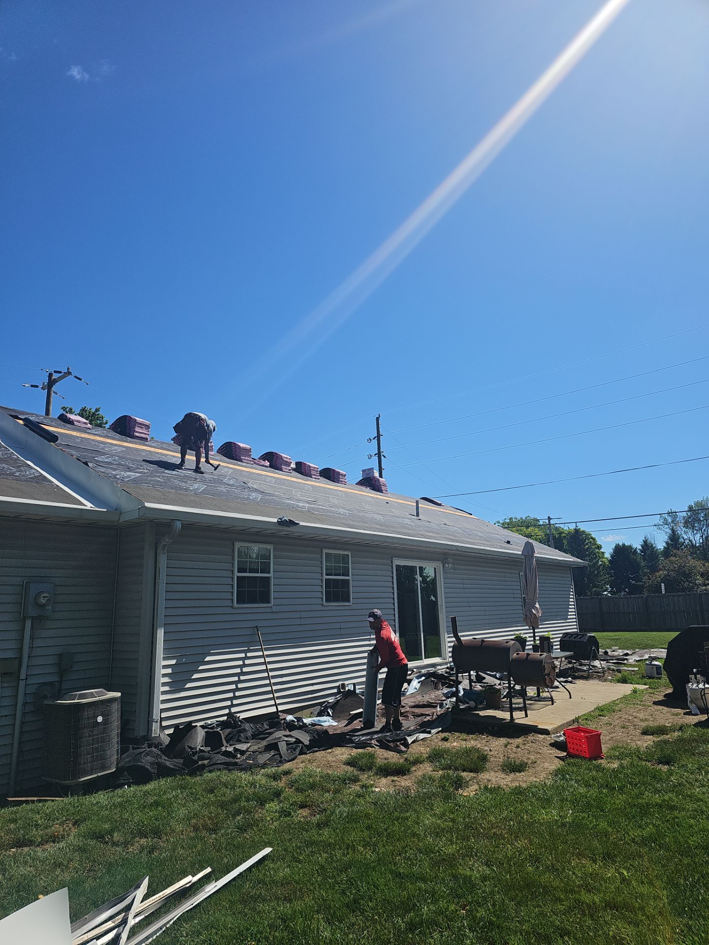 Worker on a house roof near solar panels under a bright blue sky.