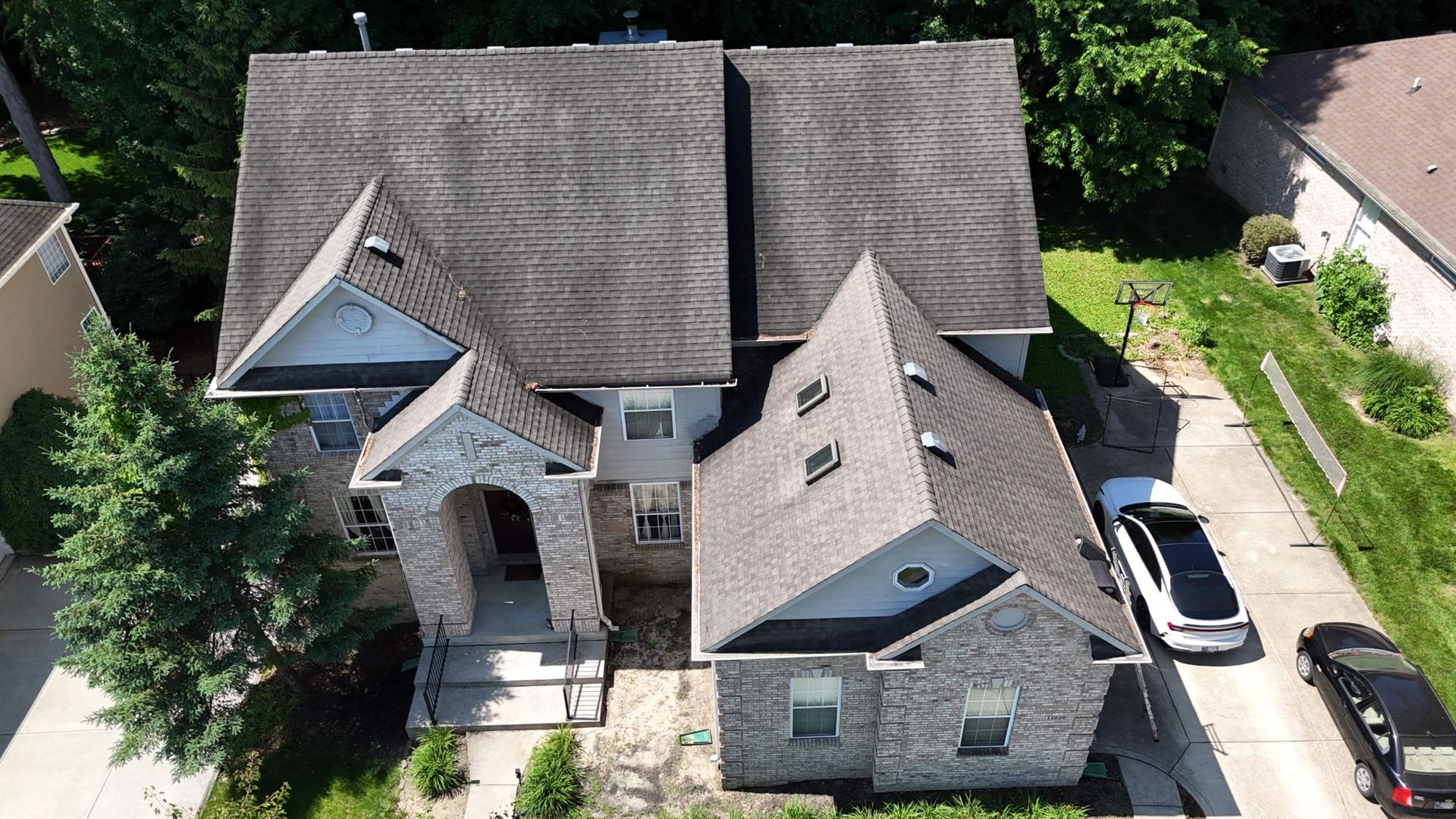 Aerial view of a large house with dark gray roofs, a front driveway, and two parked cars.