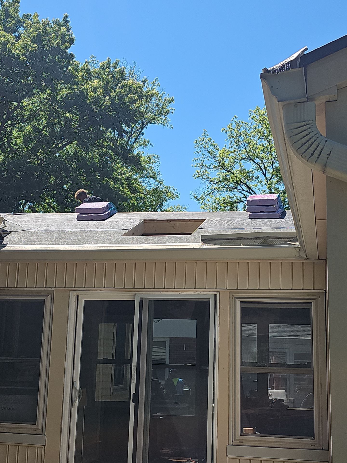 House roof with two purple roof vents against a blue sky and trees