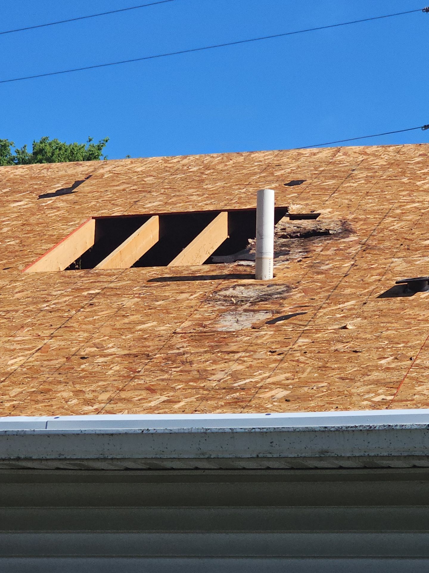 Roofer’s plywood roof with a vent pipe and two open skylight cutouts under blue sky