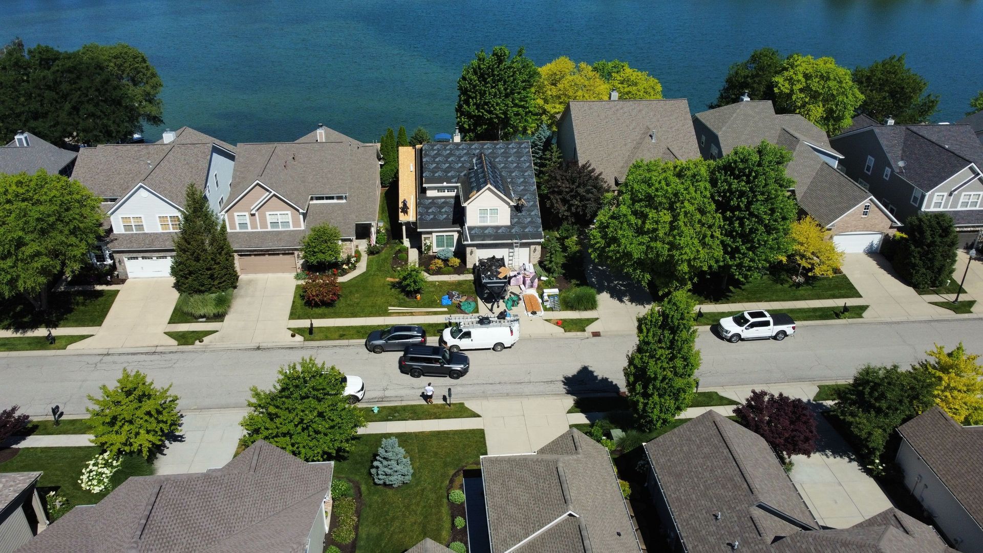 Aerial view of a suburban neighborhood beside a lake, with houses, trees, and parked cars.