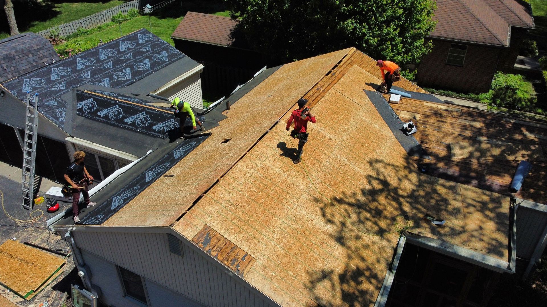 Worker on a roof installing plywood sheathing on a house under construction.