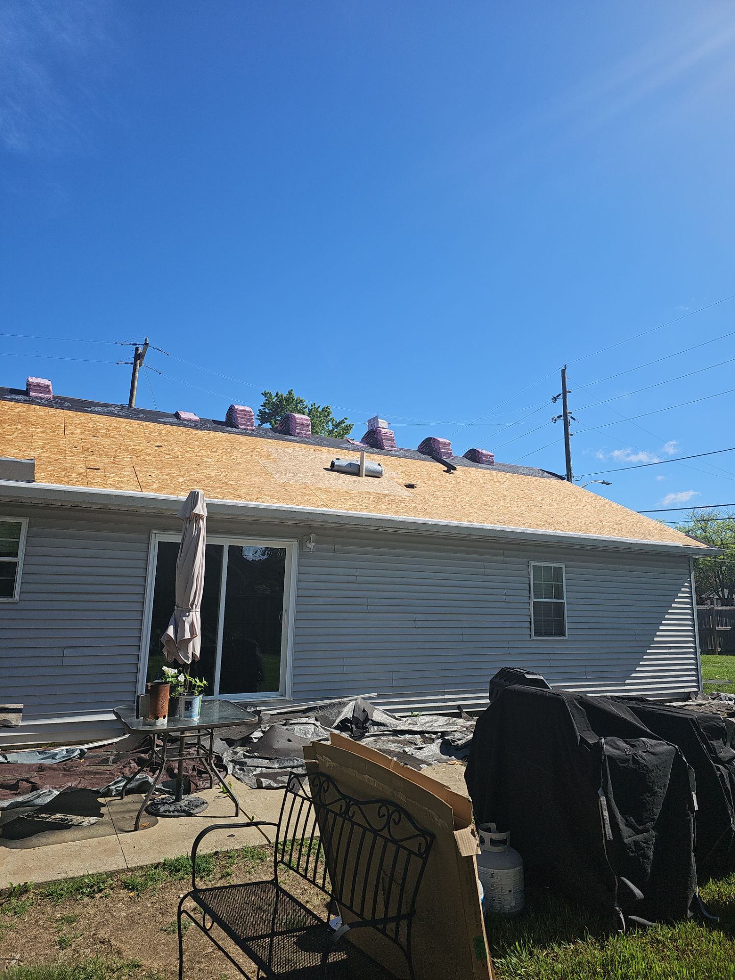 Damaged house exterior with torn roof and debris in the yard under a clear blue sky