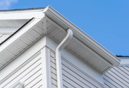 White house siding and roof eaves with a rain gutter against a blue sky