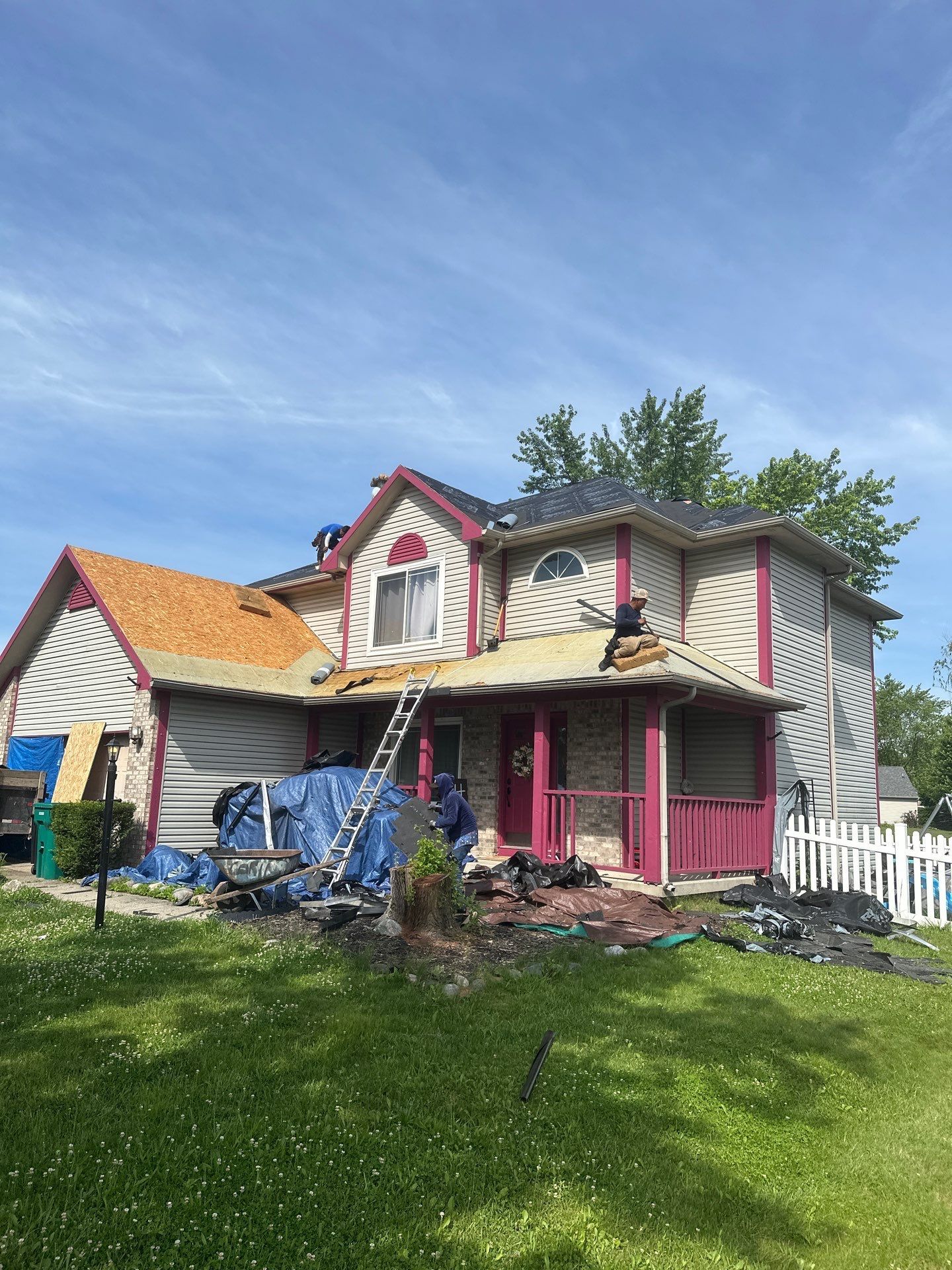 Damaged two-story house with striped siding, pink porch, and debris on the lawn under a blue sky