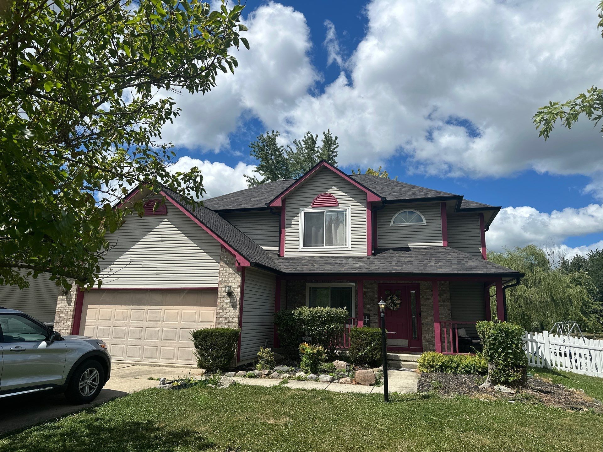 Two-story house with beige siding, pink trim, a front porch, garage, and a partly cloudy blue sky.