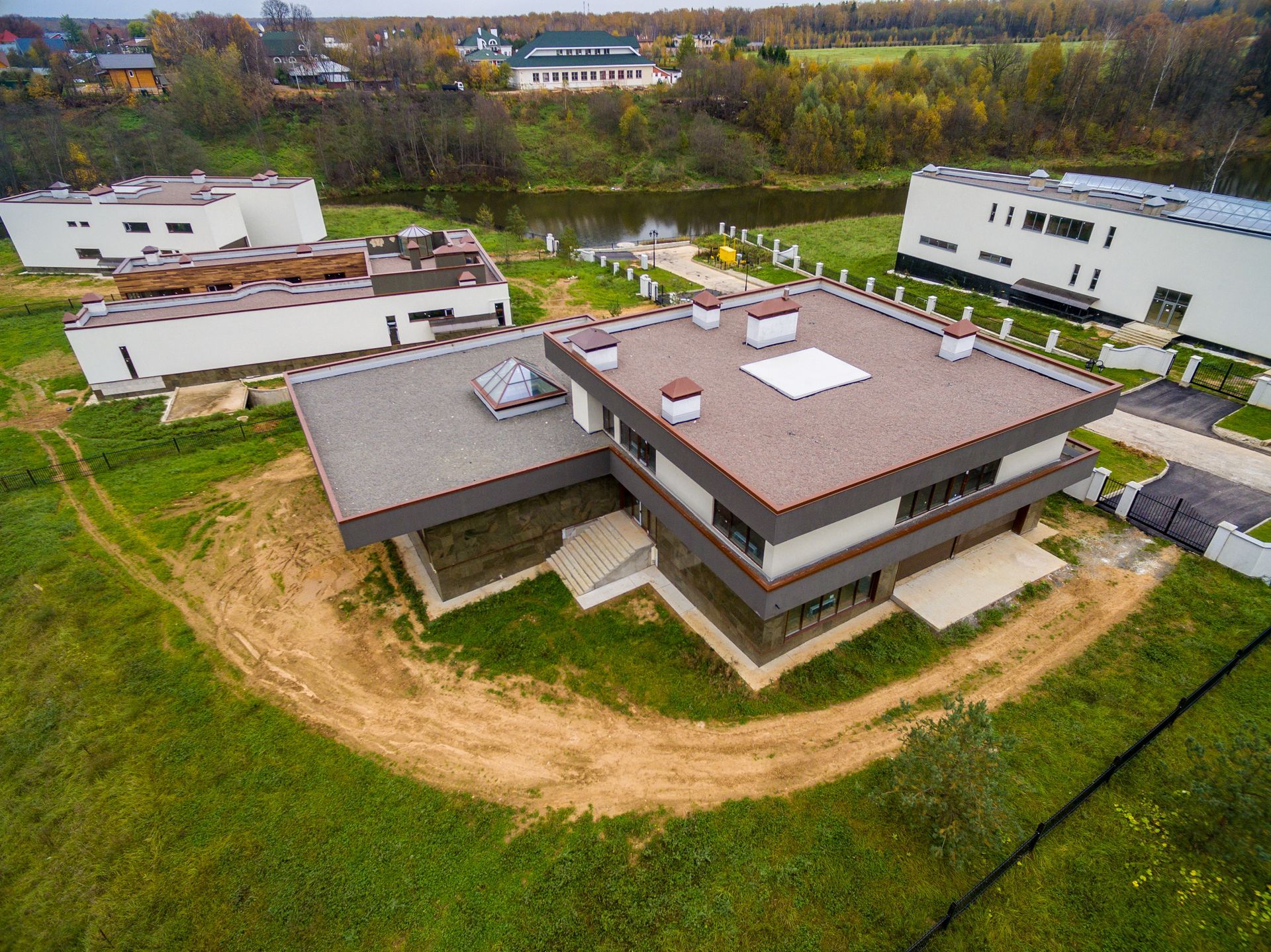 Aerial view of a modern house with a brown roof, surrounded by green lawn and neighboring buildings.